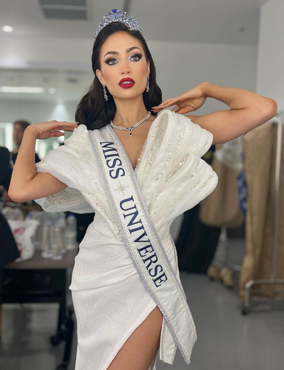 R'Bonney posing with her arms on her shoulders, white gown, Miss Universe crown and sash