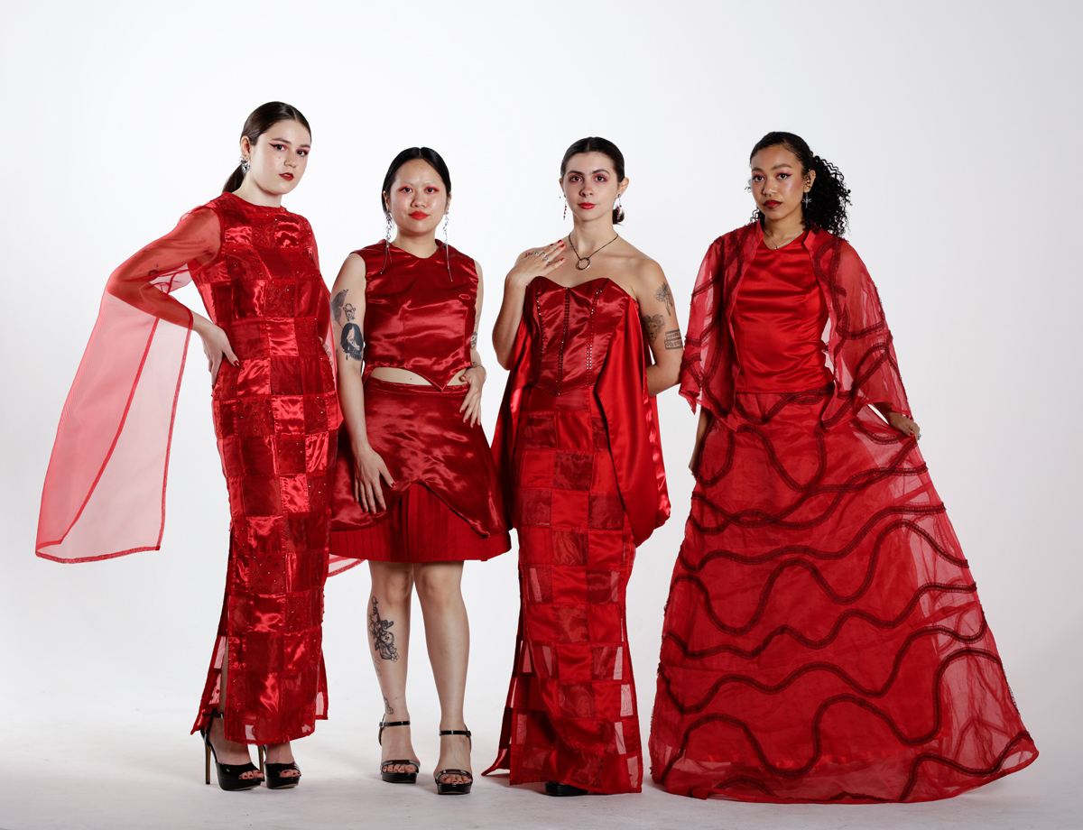 Four models wear an assortment of red garments in stylish poses grouped in front of a clean white background.