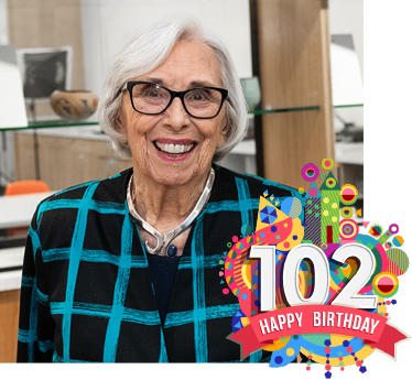 Billie Gough on her 100th birthday, smiling, white hair, glasses, black and turquoise jacket