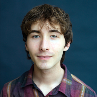 Noah Garcia facing forward and smiling. He has short brown hair and wears a dark plaid shirt.