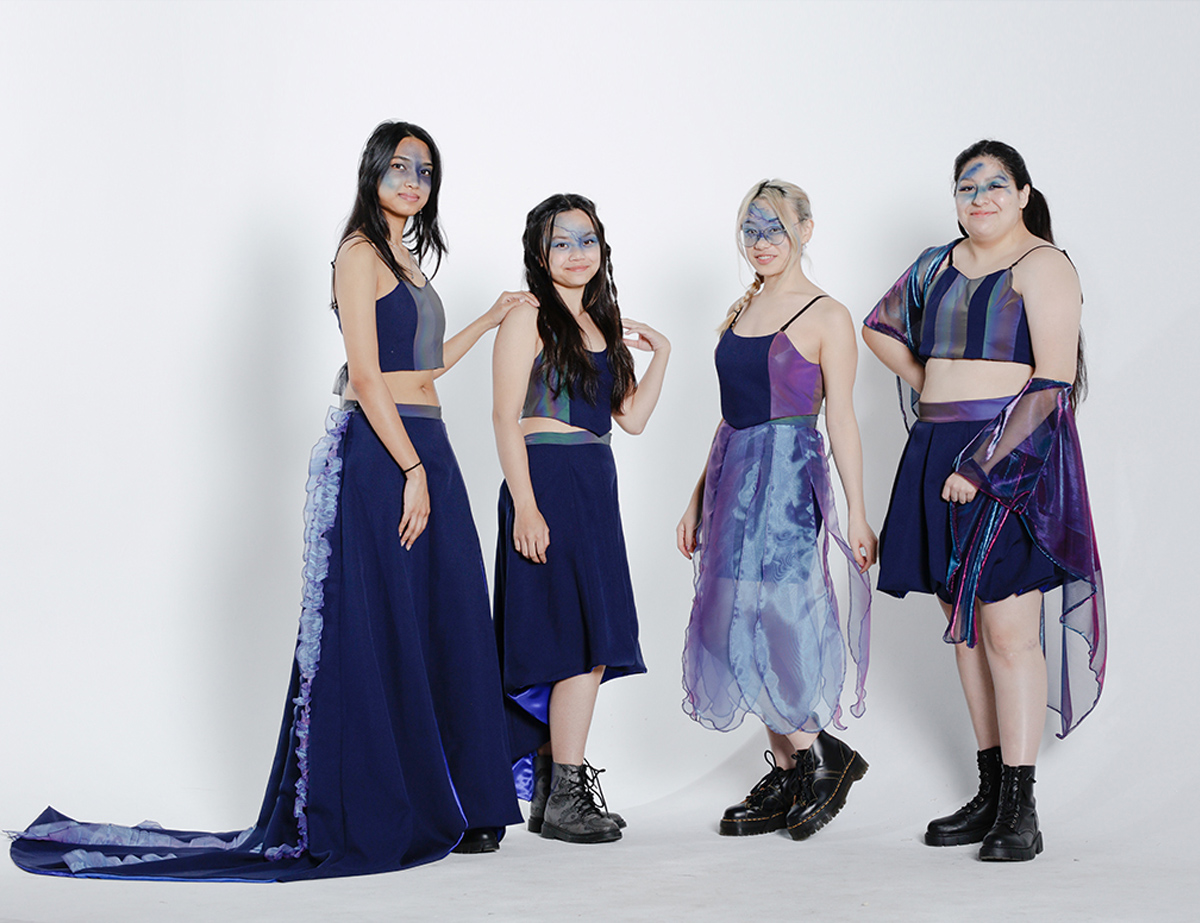 Four models wearing blue and reflective materials, that play with the light, in a white background photoshoot studio.