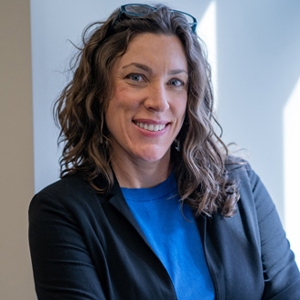 Karen Hutzel facing forward and smiling. She has long wavy brown hair and wears a blue shirt.