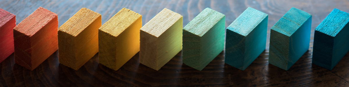 Blocks of wood in a rainbow array of colors lined up next to each other.