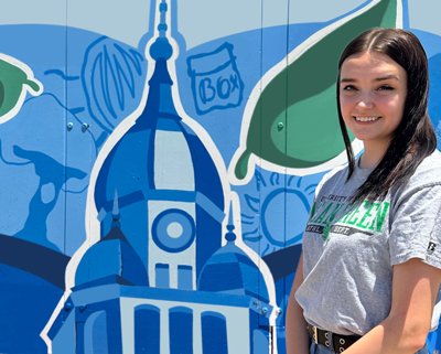 Kaci looking forward in a UNT T-shirt with a blue, white and green mural in the background