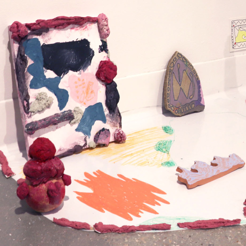 Small colorful paintings and sculptures arranged on white decorated vinyl on gallery floor
