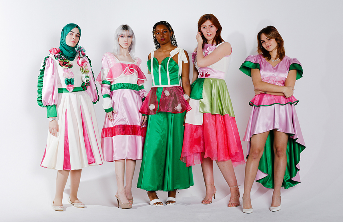 Five models wearing pink, green, and white dresses and standing on white studio background.