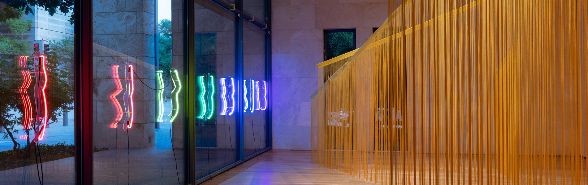 View from inside of the Nasher Gallery looking at the neon sculptures and a large fringed installation