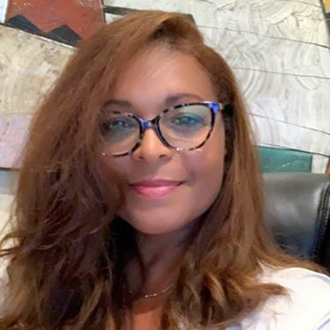 Felicia smiling at the camera, head-and-shoulders, long brown hair, glasses