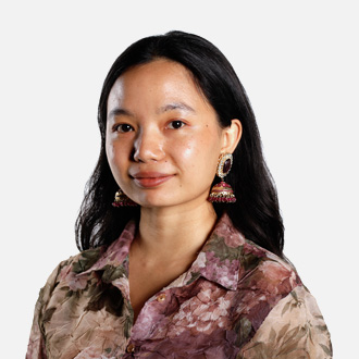 Numa facing forward, smiling, long dark hair, earrings, brown and white shirt