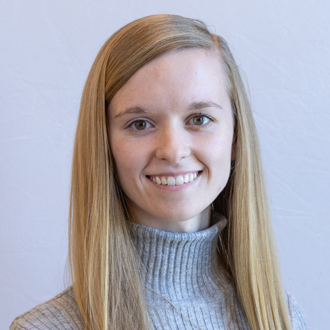 Macy facing forward, smiling, long blonde hair, blue shirt