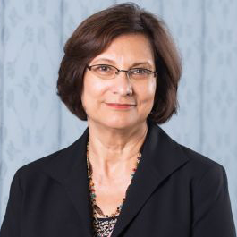 Salwa Mikdadi smiling, brown hair, wearing glasses, multi-colored necklace, dark jacket