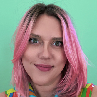 Megan, head-and-shoulders image, smiling at the camera, pink hair, colorful top