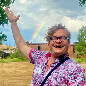 Brooks Oliver with his right hand in the air showing the rainbow above the Archie Bray buildings.