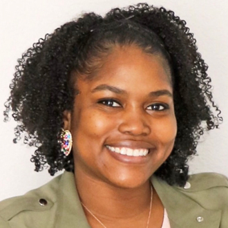 Deloya Pepe smiling, short curly hair, large earrings, olive-colored top