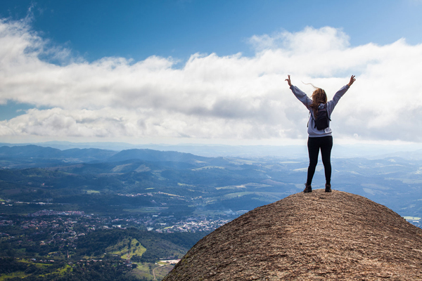 Person high up on a hill with arms up, background is a city below