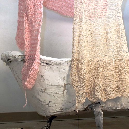 Detail of an art installation showing part of a bathtub and knitted scarves in pink and white