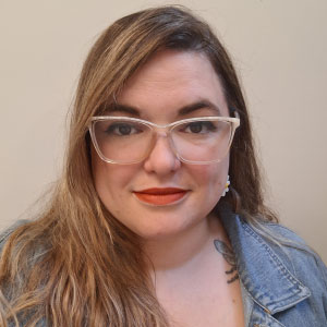 Robyn in a blue jean jacket. She has long light brown hair, wears glasses.