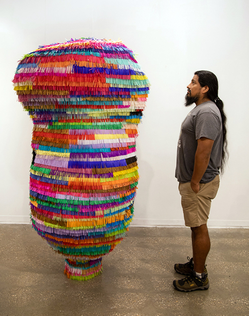 Saxon Martinez standing in profile with a piñata that is taller than he.