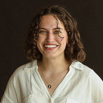 Gina facing forward smiling, medium-length curly hair, beige shirt