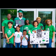 Family all wearing UNT t-shirts surrounding the graduate in his regalia