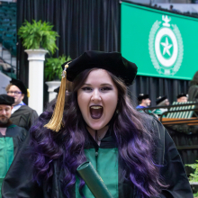 Graduate student showing excitement with diploma as they walk back to their seat at the Spring 2023 commencement ceremonies.