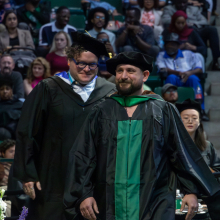 Graduate student Eric Grasham walking across the stage to receive his M.F.A. in Studio Art: Ceramics at the Spring 2023 commencement ceremonies.
