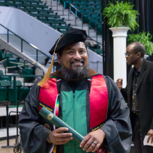 Graduate student smiling with diploma as they walk back to their seat at the Spring 2023 commencement ceremonies.