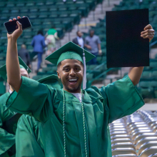 Undergraduate student cheering and celebrating as they walk out if the UNT Coliseum with their diploma from UNT CVAD.