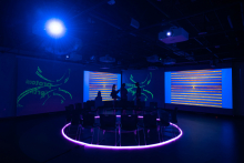 The New Media cave with all projectors on and chairs set up in a circle in the center of the room with a pink LED rope light forming a circle around the chairs.