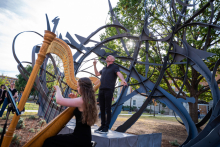 Countertenor Daniel Bubeck and harpist Ruth Mertens performing while the sun peaks through tree branches and the Shadow Garden sculpture.