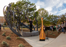 Countertenor Daniel Bubeck with arms outstretched to the sky and harpist Ruth Mertens strumming during their performance at the dedication of the "Shadow Garden" sculpture.