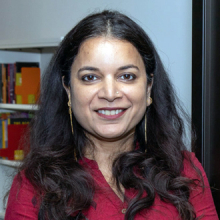 Manisha facing forward, smiling, long black wavy hair, maroon top