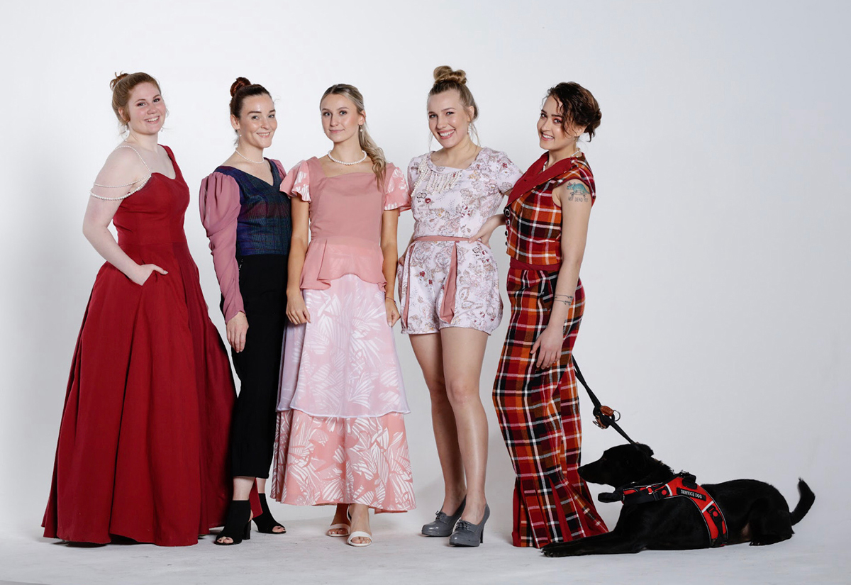 Collection image of all five looks lined up with female models a service dog for the model in the reversible vest and bell bottoms displaying the burgundy, dusty rose, teal, purple, mustard yellow, black, and white outfits.